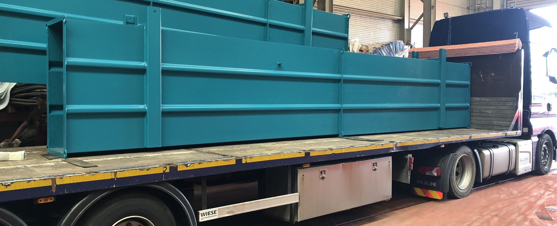 Großes beschichtetes türkisfarbenes Bauteil auf Ladefahrzeug in Produktionshalle