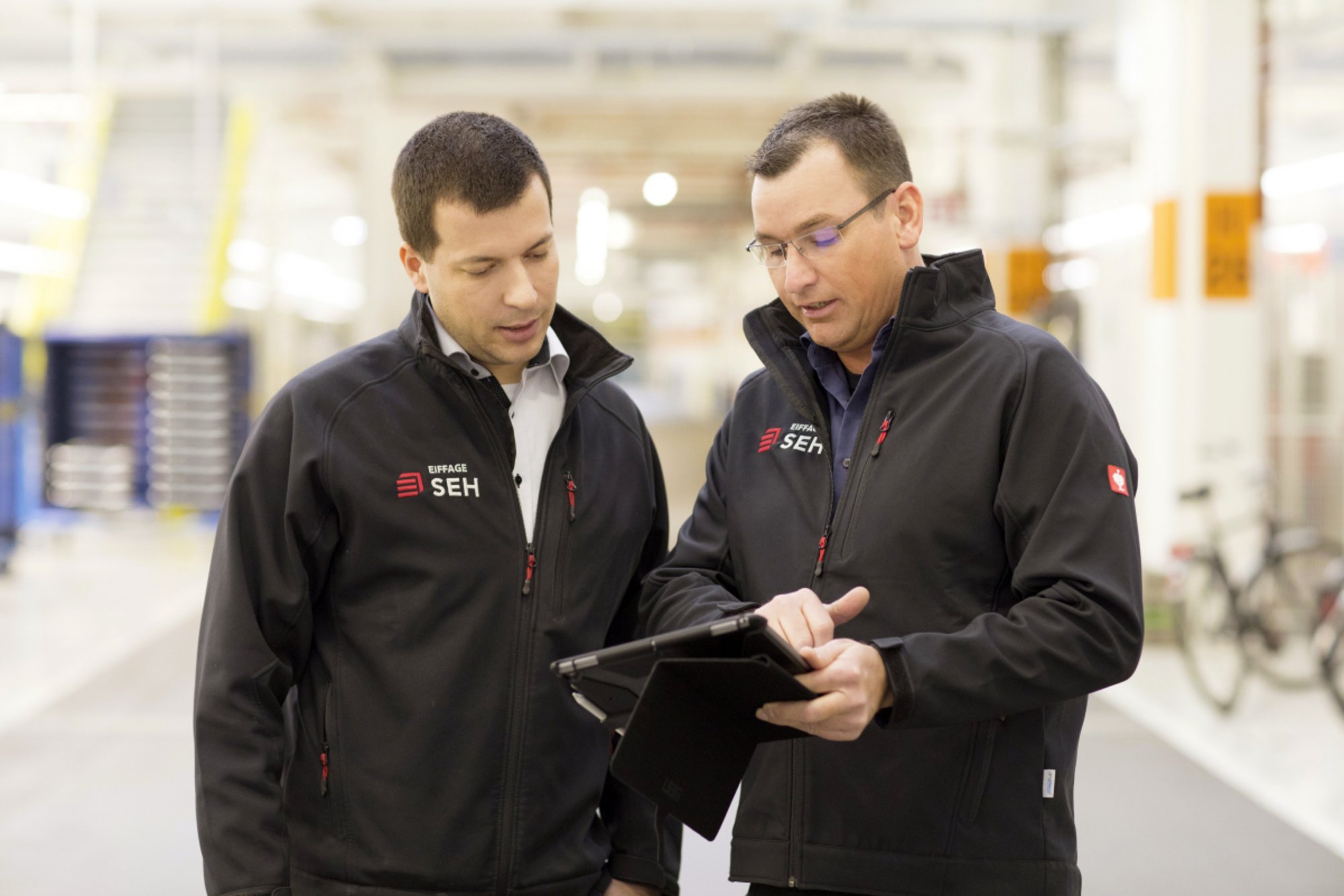 Zwei Mitarbeiter in Arbeitskleidung bei der Besprechung von Inhalten auf einem Tablet