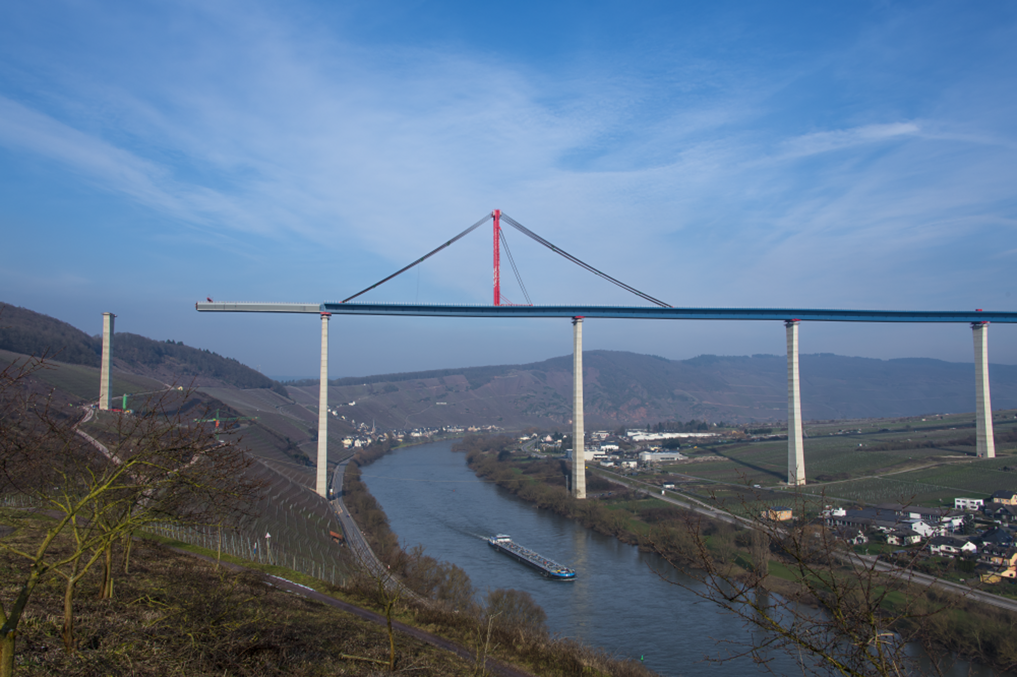 Hochmoselbrücke bei Tageslicht, ein Schiff fährt im Fluss darunter