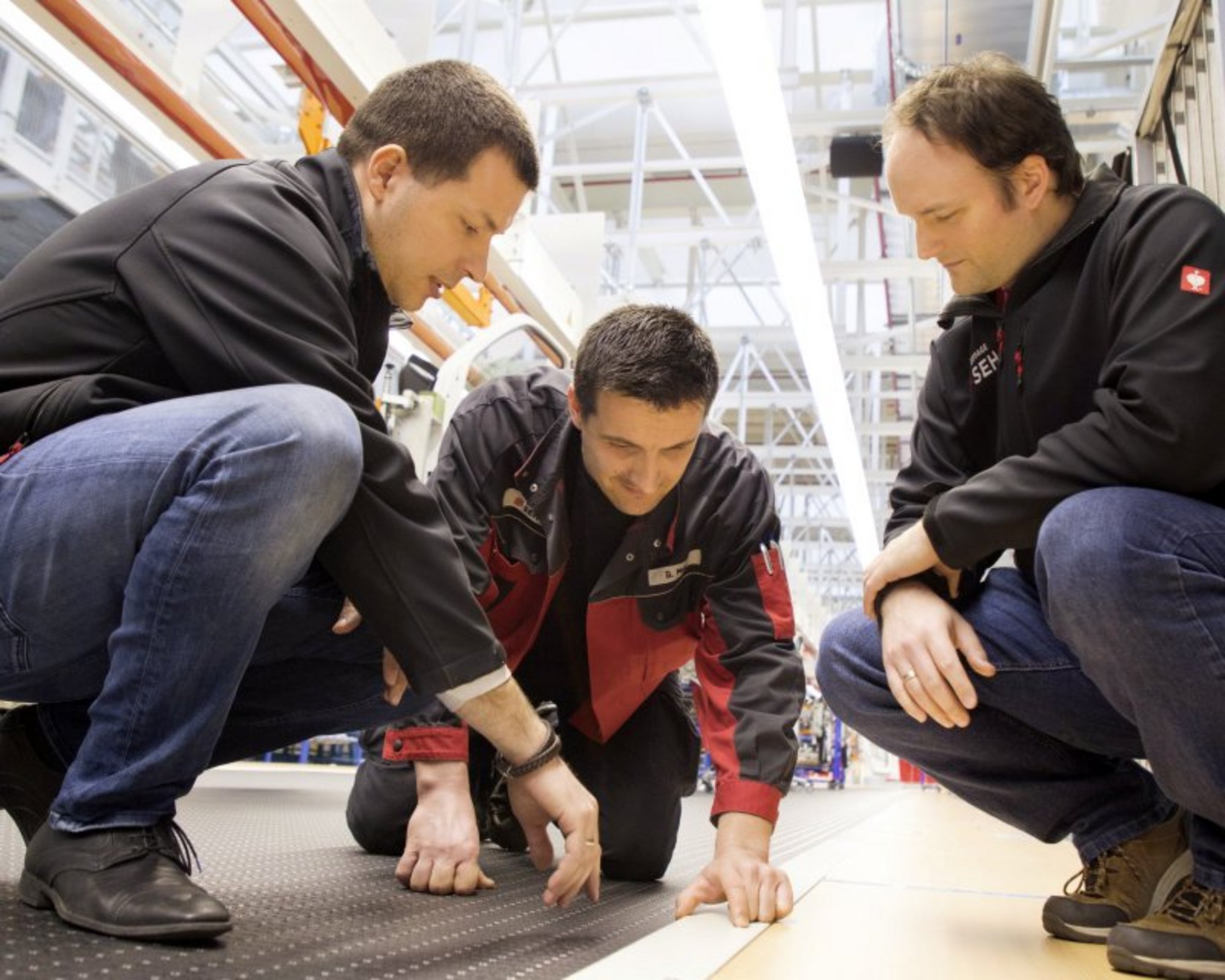 Drei Mitarbeiter betrachten eine Leiste auf dem Boden