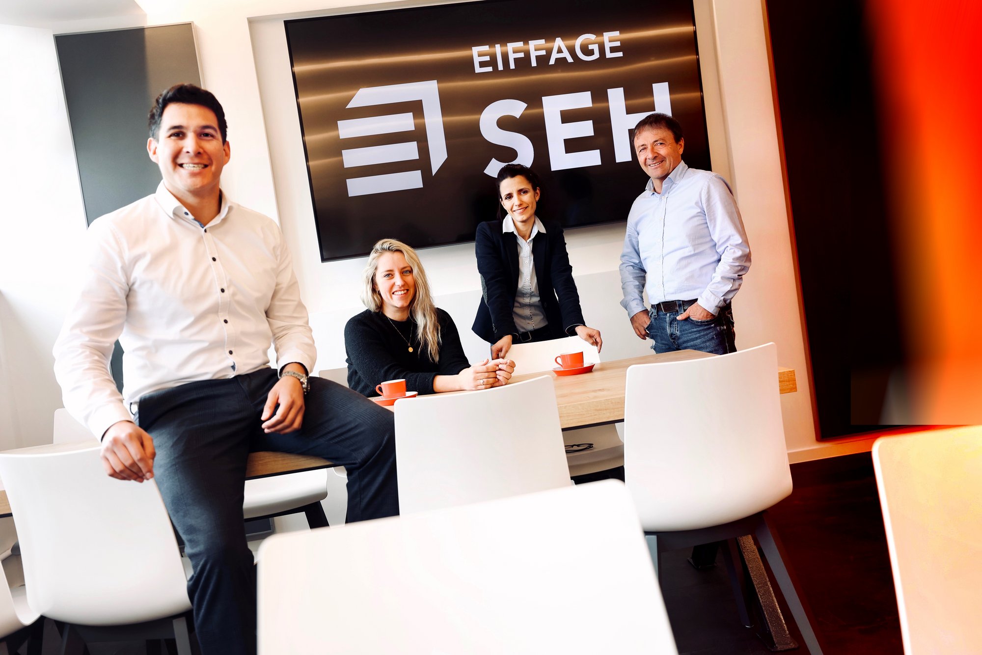 Vier Mitarbeiter in einem Büroraum, lächelnd zur Kamera gewandt – im Hintergrund ein Bildschirm mit dem Logo und Namen „Eiffage SEH“