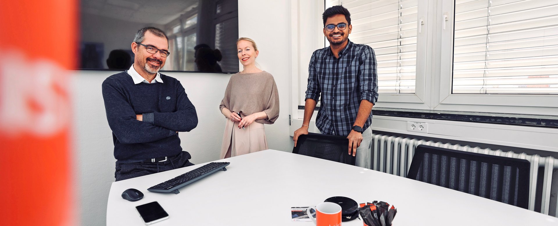 Gruppenfoto von drei Mitarbeitenden im Besprechungsraum, freundlich in die Kamera blickend