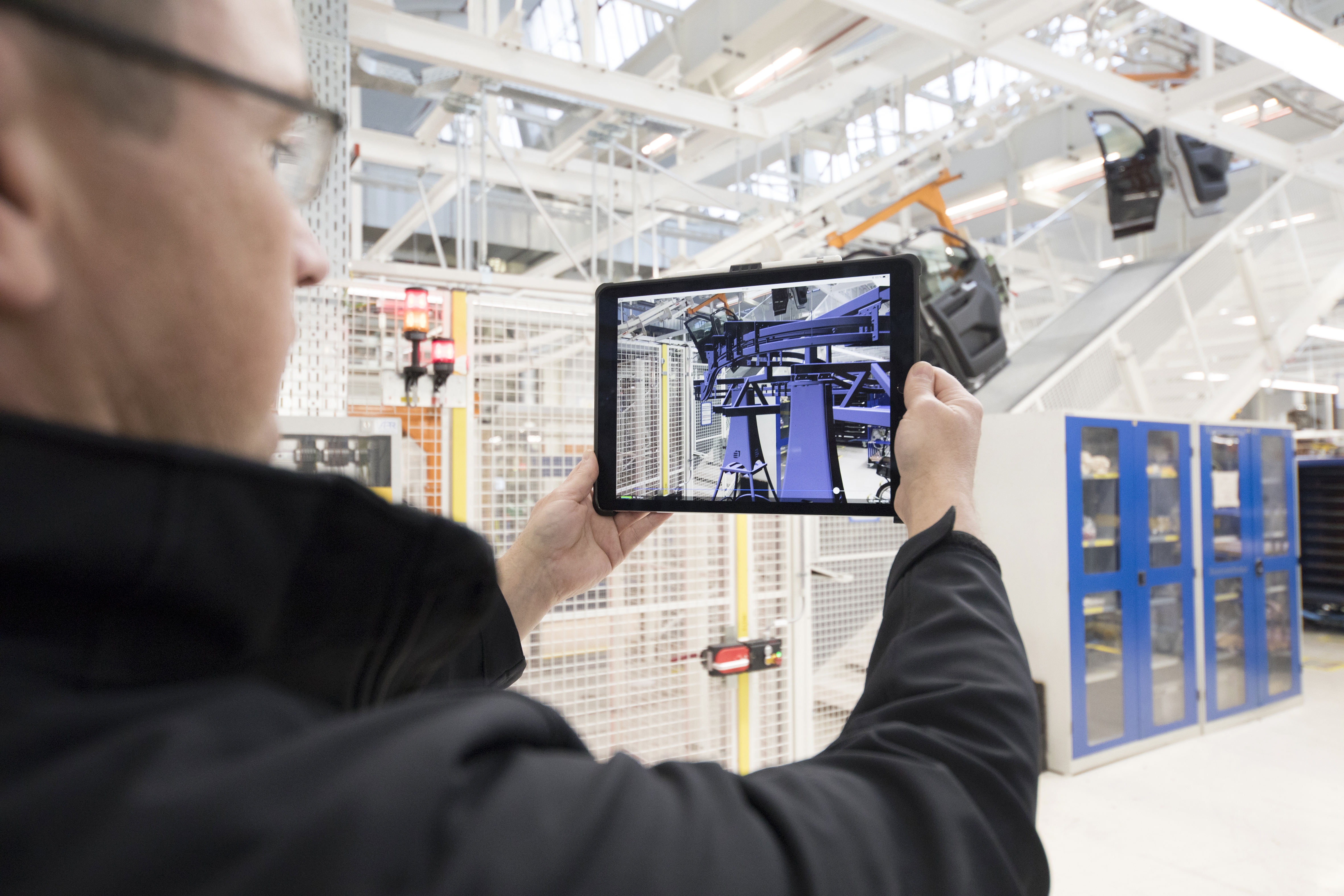 Mitarbeiter hält Tablet mit sichtbarem Bildschirm, auf dem ein virtuelles blaues Konstrukt in die reale Umgebung eingeblendet ist